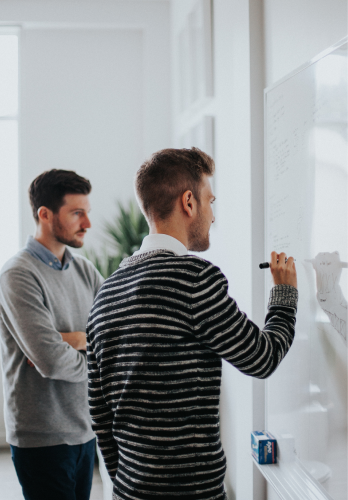 Dois homens concentrados idealizando um novo projeto em frente a um quadro branco
